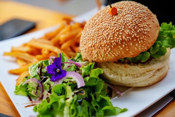 A mouthwatering burger featuring a sesame seed bun, fresh lettuce, ripe tomato, and crunchy onion, served with crispy fries that perfectly complement this delightful meal.