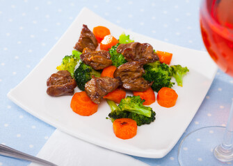 Roasted chicken hearts served with colorful garnish of green broccoli and orange carrots on white dish..