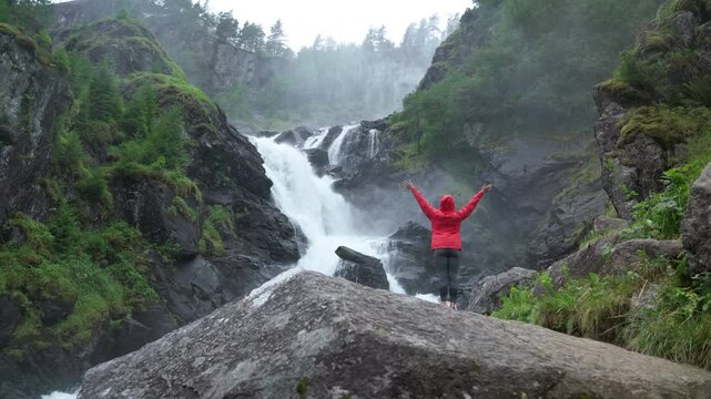 Woman trekker dressed bright red waterproof jacket with enjoying L&aring;tefossen Waterfall, Norway. 4K footage of Beauty of Nature.