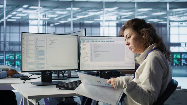 Employee overseeing server room, reading documentation paperwork, troubleshooting hardware. Supervisor doing inspection in server hub, reading technical files at computer desk, camera B