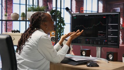 Frustrated day trader feeling upset, looking at PC screens showing falling stock prices, red charts and losses. Investor overwhelmed while looking at drop in stock exchange shares on monitor, camera B