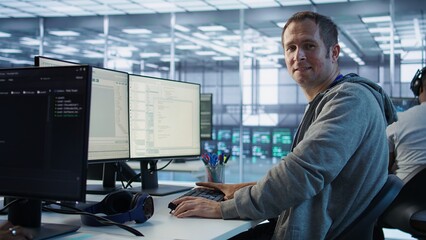Portrait of smiling engineer inspecting server rows in data center. Happy man supervising supercomputers providing processing and memory resources for various workloads, camera B
