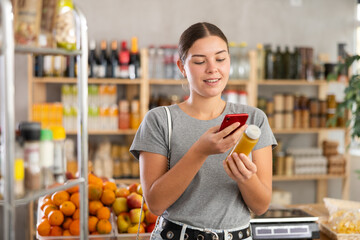 Youth girl customer at shop scan QR code on smoothie package using phone camera. Client inspect...