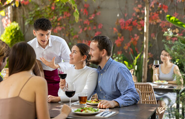 Young waiter talking to restaurant guests - taking orders for food and drinks
