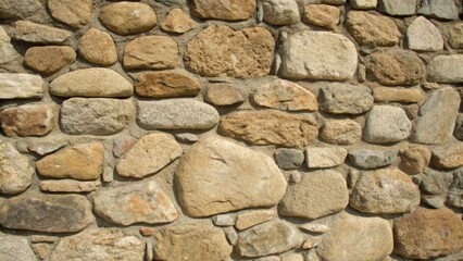 A medium closeup of a stone wall displaying various sized stones fitted snugly together without mortar emphasizing the ingenuity of using locally sourced materials for stability