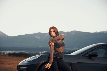 Woman in metallic outfit posing confidently beside a luxury car in natural scenery