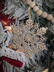 Close-up of frosted evergreen Christmas tree branch decorated with wooden bead garland and golden ornaments