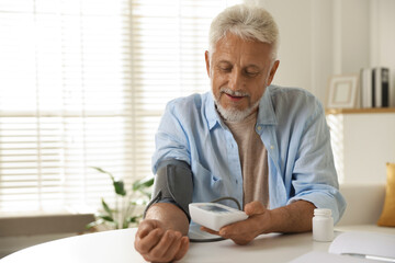 Senior man measuring blood pressure at table indoors
