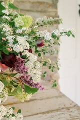 Floral arrangement in white textured compote with pink peonies, irises spirea, tulips, hydrangeas, lilacs