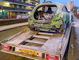 A heavily damaged car with crumpled metal, shattered windows, and missing parts sits tilted on a...