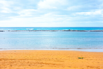 Serene beach scene with golden sand, calm turquoise waters, and gentle waves under a cloudy sky, evoking a tranquil and peaceful coastal atmosphere, perfect for relaxation and nature-themed visuals