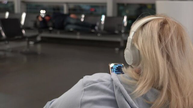 Vienna, Austria - January 19, 2025: A female passenger wearing headphones in an airport terminal. Waiting for a flight before boarding. A man sleeping on the seats in the waiting room.
