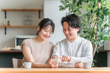 リビングダイニングでスマホを見る若いアジア人カップル

