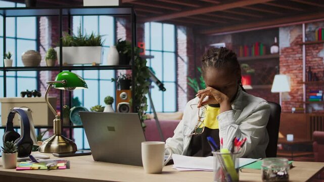 Overworked freelancer in apartment trying to relax, closing eyes after working too much on laptop. Remote worker feeling eye strain, getting overstimulated while working from home, camera A