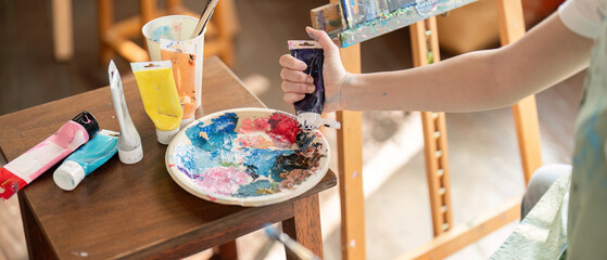 Focused artist squeezing paint tubes onto a palette while preparing to create her next work in a bright studio