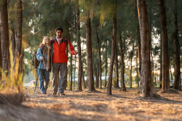Fototapeta premium Two hikers standing in a forest, dressed in winter clothing with trekking poles and backpacks. A serene outdoor adventure showcasing nature, exploration, and friendship.