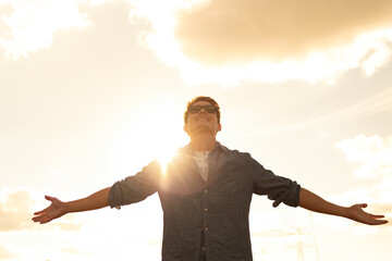 Young man in the sunset looking up to the sky with arms outstretched feelings of joy, happiness and freedom 