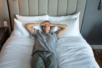 Tired, stressed exhausted man lying in bed hand over face	