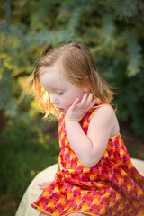 Portrait of female child wearing bright red dress sitting in natural garden setting