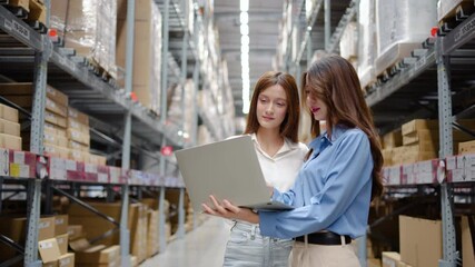 In a bustling warehouse filled with shelves of products, two women share insights and strategies while working on a laptop computer, demonstrating teamwork and efficiency in their tasks. - Powered by Adobe