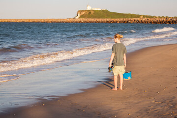 Pre-teen boy walking on beach carrying bait bucket for fishing