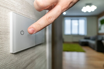close-up finger turns on the light on the touch switch. A white modern light switch on a white wall. modern design.