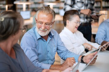 Senior man and woman using tablets in a library. Elderly man and woman enjoying technology. Group of seniors in a library setting, engaging with tablets and social media, learning modern technology.