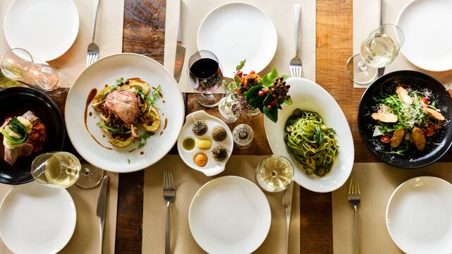 Aerial view of a dining table set with plates of pasta, salad, and meat dishes. Elegant food course with wine. The dining experience. Top view of dinning table set. Long served restaurant table