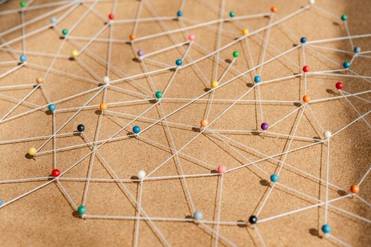Colorful pins connected by strings on corkboard. Network of pins and strings. Pins and strings forming a web. Strings and pins creating connections. Connection background, business network background.