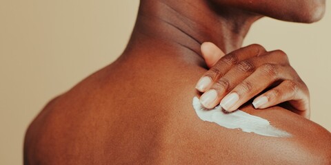 Close-up of a woman applying lotion to her shoulder. Black woman applying cream on her shoulder. Skincare routine. Beauty product, applying lotion on shoulder.