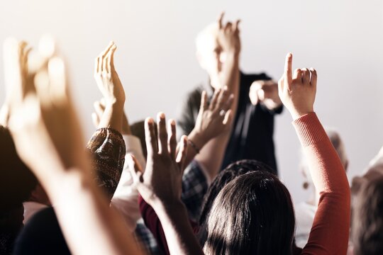 A diverse group of people raising hands in a classroom or seminar setting, with a focus on participation and engagement. Hands raised, diverse group, active learning.