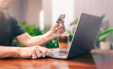 Man holding credit card, involved in online shopping at home, happy male shopper purchasing goods or services in internet store.