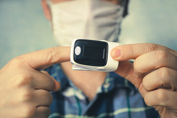 Self-diagnosis at home - male finger pulse oximeter - self-monitoring of blood saturation on blue background