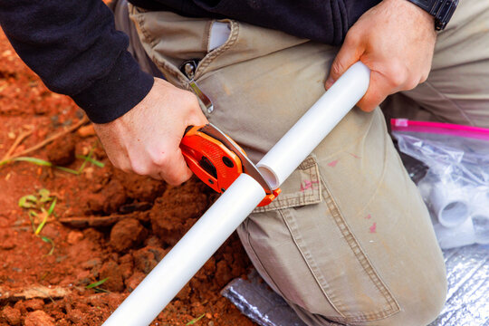 Plumber is using cutting tool to accurately shorten PVC pipe in dirt area during plumbing water line installation