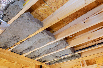 Workers install insulation between wooden beams in building, enhancing energy efficiency, comfort during construction new home