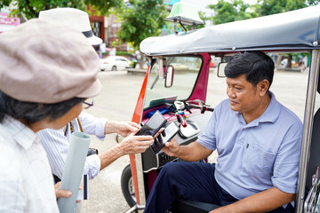Senior tourist man poses paying the fare to the Tuktuk Thailand taxi driver by smart phone. Senior tourist concept
