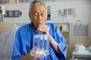 Senior asian man using incentive spirometer device for breathing exercise rehabilitation to recover from lung cancer after surgery due to heavy smoking in hospital bed