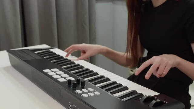 Female musician playing a midi controller keyboard, composing electronic music in a home studio setting, utilizing modern technology for music production
