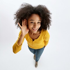 An attractive black woman with a hand near her ear, moving closer to the camera to listen from a top angle on a white background.