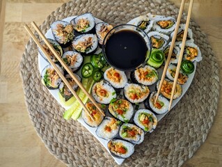 Assorted sushi rolls arranged on heart shaped platter with soy sauce and chopsticks