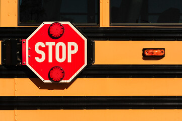 Close-up of a red stop sign with flashing red lights mounted on the side of a yellow school bus,...