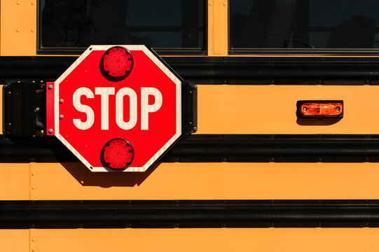 Close-up of a red stop sign with flashing red lights mounted on the side of a yellow school bus, highlighting student safety and transportation regulations in the school transportation industry