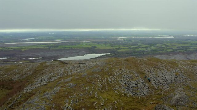 Dynamic aerial shot flying over Mullaghmore Peak, showcasing hikers and stunning Burren views