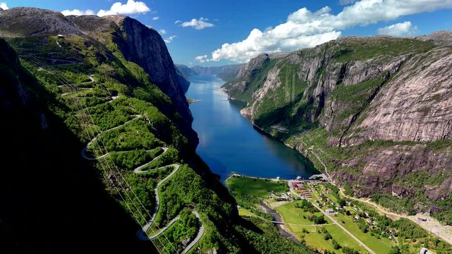 Majestic cliffs rise along the serene waters of Norways fjords, showcasing lush greenery and captivating winding roads. Lysefjord Lysebotn Norway