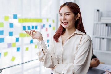 Business female employee with many conflicting priorities arranging sticky notes commenting and brainstorming on work priorities colleague in a modern office.