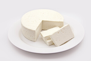 WHOLE ROUND FRESH RICOTTA CHEESE WITH CHOPPED PIECES ON DISH ON ISOLATED WHITE BACKGROUND