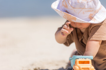 toddler boy plays on a sandy beach in a panama hat and cotton clothes in summer