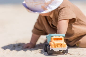 toddler boy plays on a sandy beach in a panama hat and cotton clothes in summer
