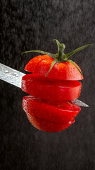 A tomato is cut into pieces in the air with drops of water on a black background, a shiny kitchen...