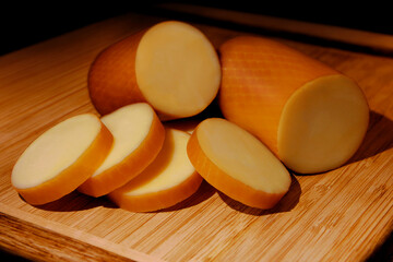 SMOKED PROVOLONE CHEESE IN A ROLL ON BOARD WITH CHOPPED PART IN FRONT ON ISOLATED WHITE BACKGROUND
